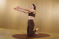 Carlotta Gagna kneeling on a mat with both arms extended forward and one foot lifted behind her in Pilates Linfodrenante®