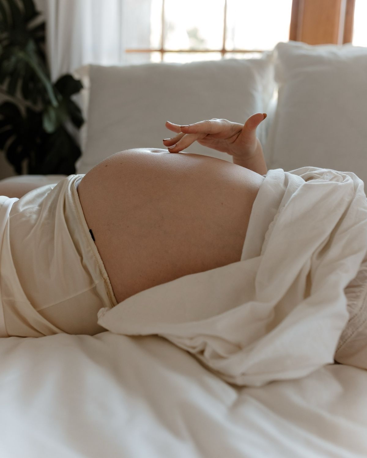 Donna incinta a letto, in posizione supina, che tocca delicatamente la pancia