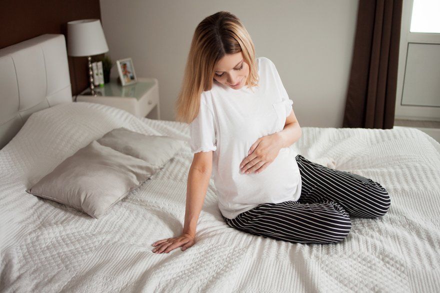 Donna incinta seduta sul fianco che si sta alzando dal letto
