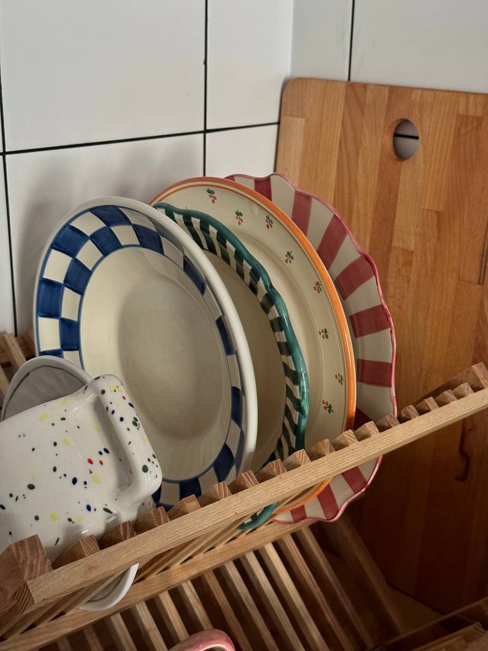 Schiera di piatti in ceramica con decorazioni colorate riposti su un poggiapiatti in legno