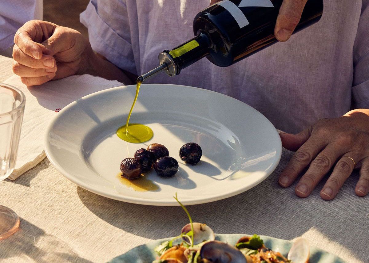 Olio extravergine di oliva versato su olive nere in un piatto bianco, condimento antinfiammatorio naturale della dieta mediterranea ricco di polifenoli