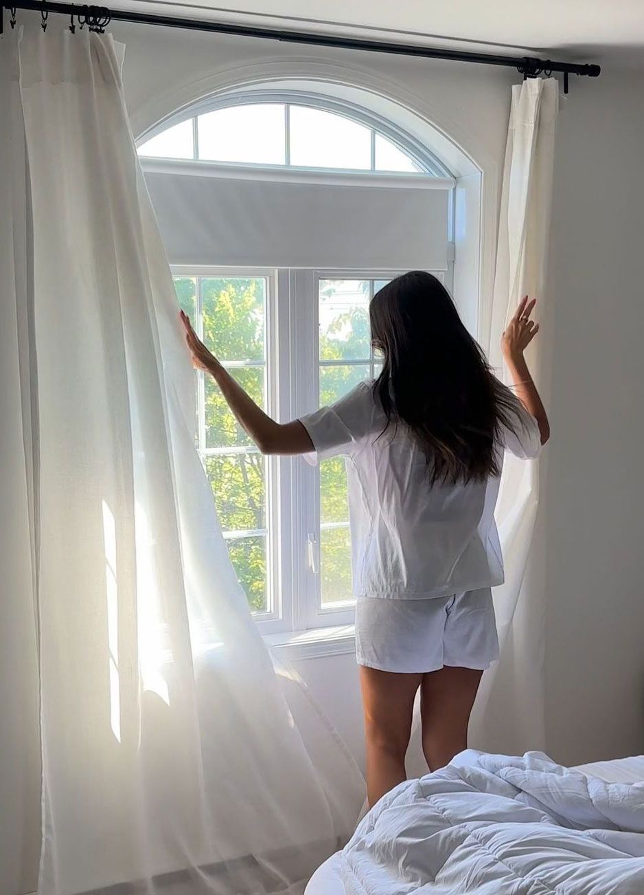 Ragazza in piedi davanti alla finestra che apre le tende dopo essersi svegliata