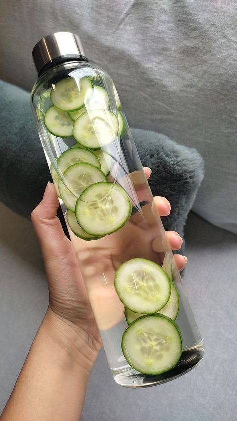 womans hand holding a water bottle with cucumber
